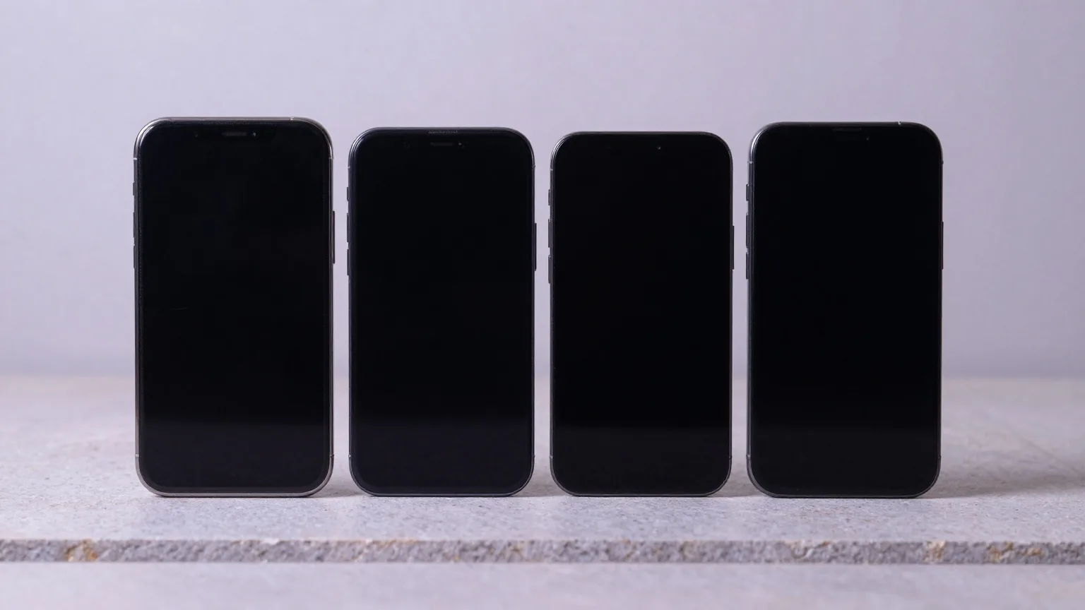 Vier Smartphones liegen mit der Rückseite nach oben nebeneinander auf einer hellen Steinplatte