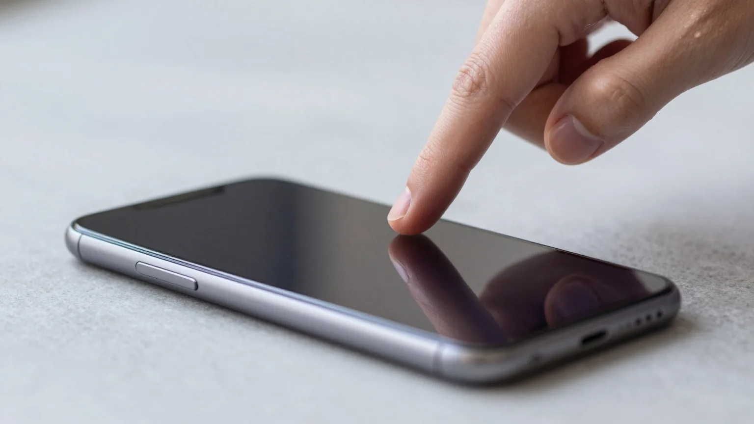 Zeigefinger schwebt über dem dunklen Glas eines Smartphones, das auf einer hellgrauen Steinplatte liegt
