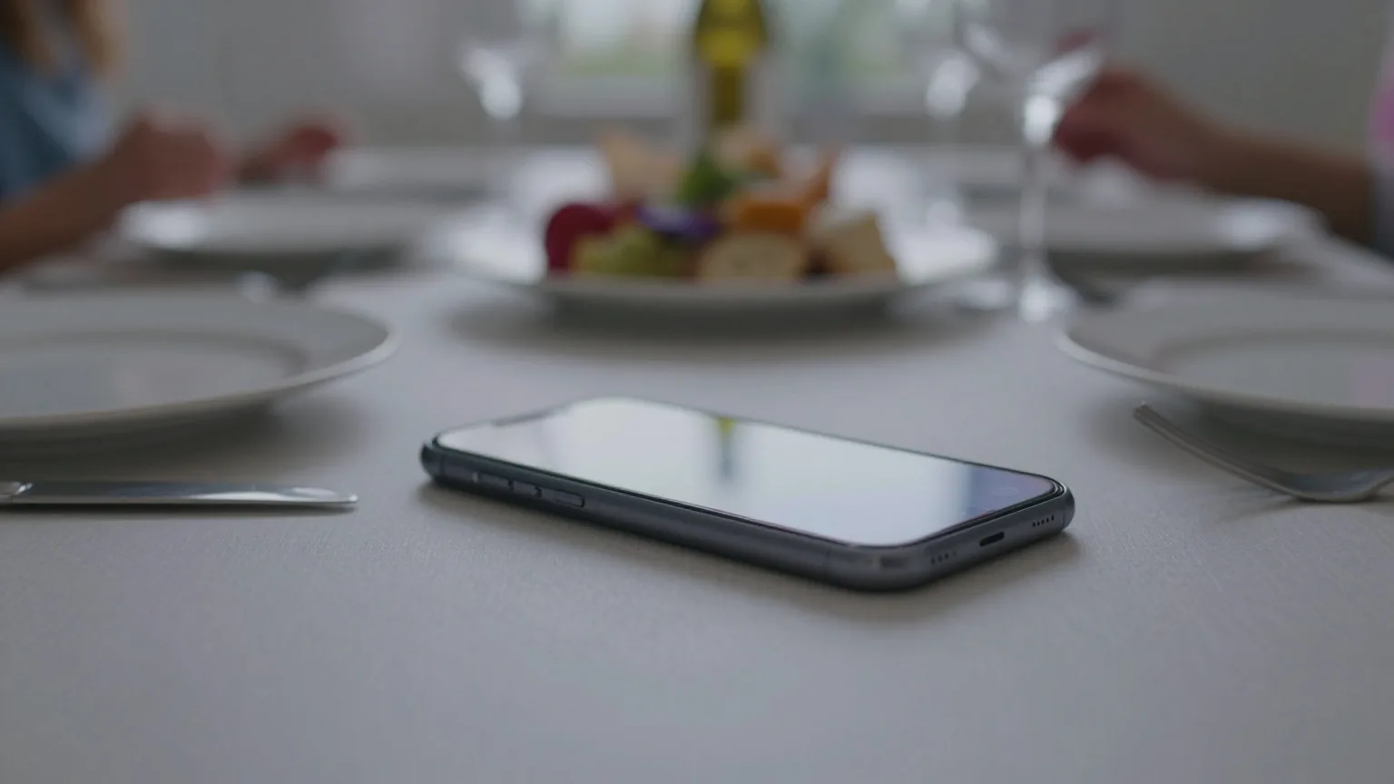 Vibrierendes Smartphone liegt mit dem Display nach unten auf einem gedeckten Abendbrottisch zwischen Tellern und Besteck
