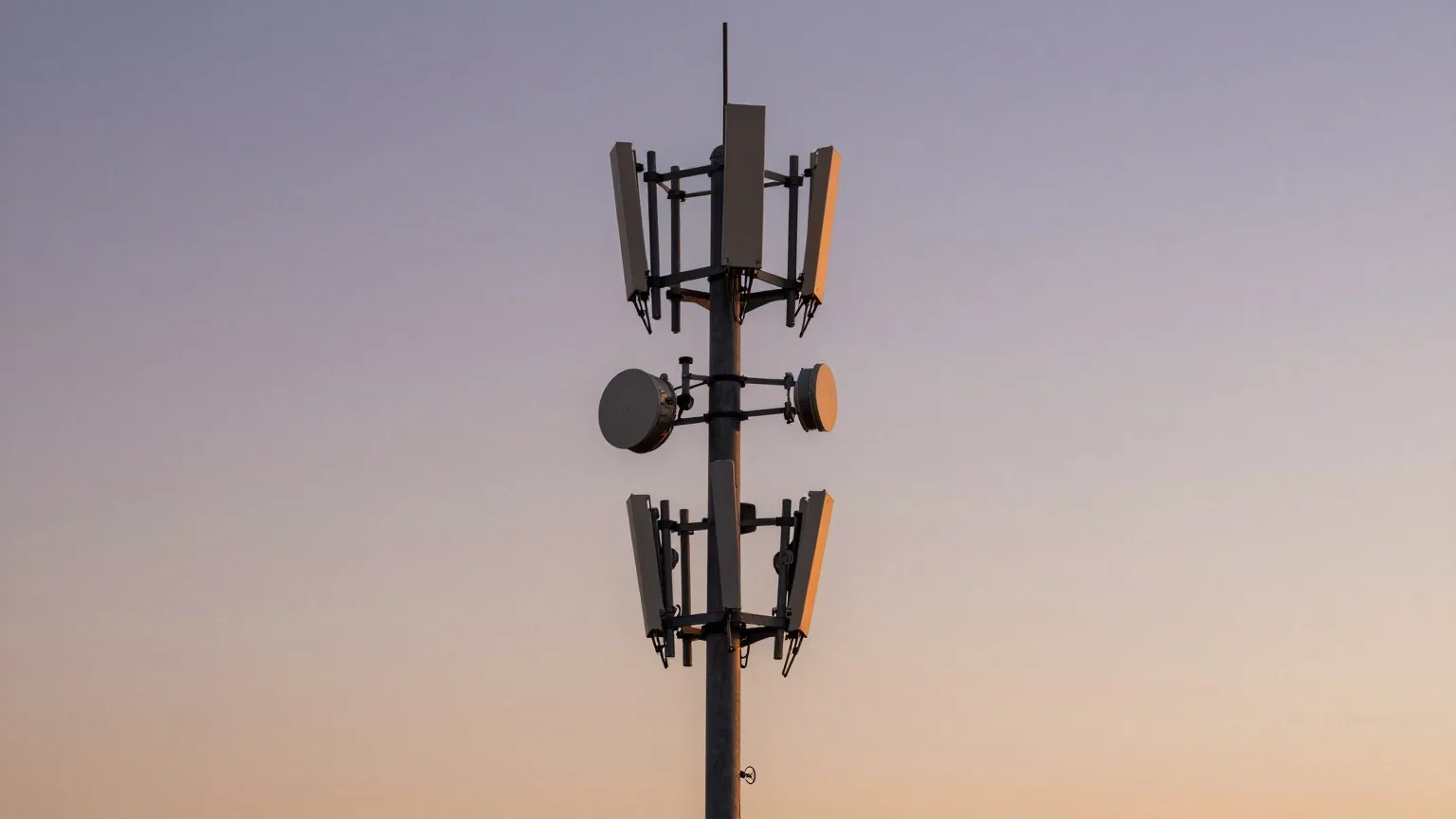 Stahlmast mit vielen unterschiedlichen Antennen, von unten fotografiert vor einem violett-orangen Abendhimmel