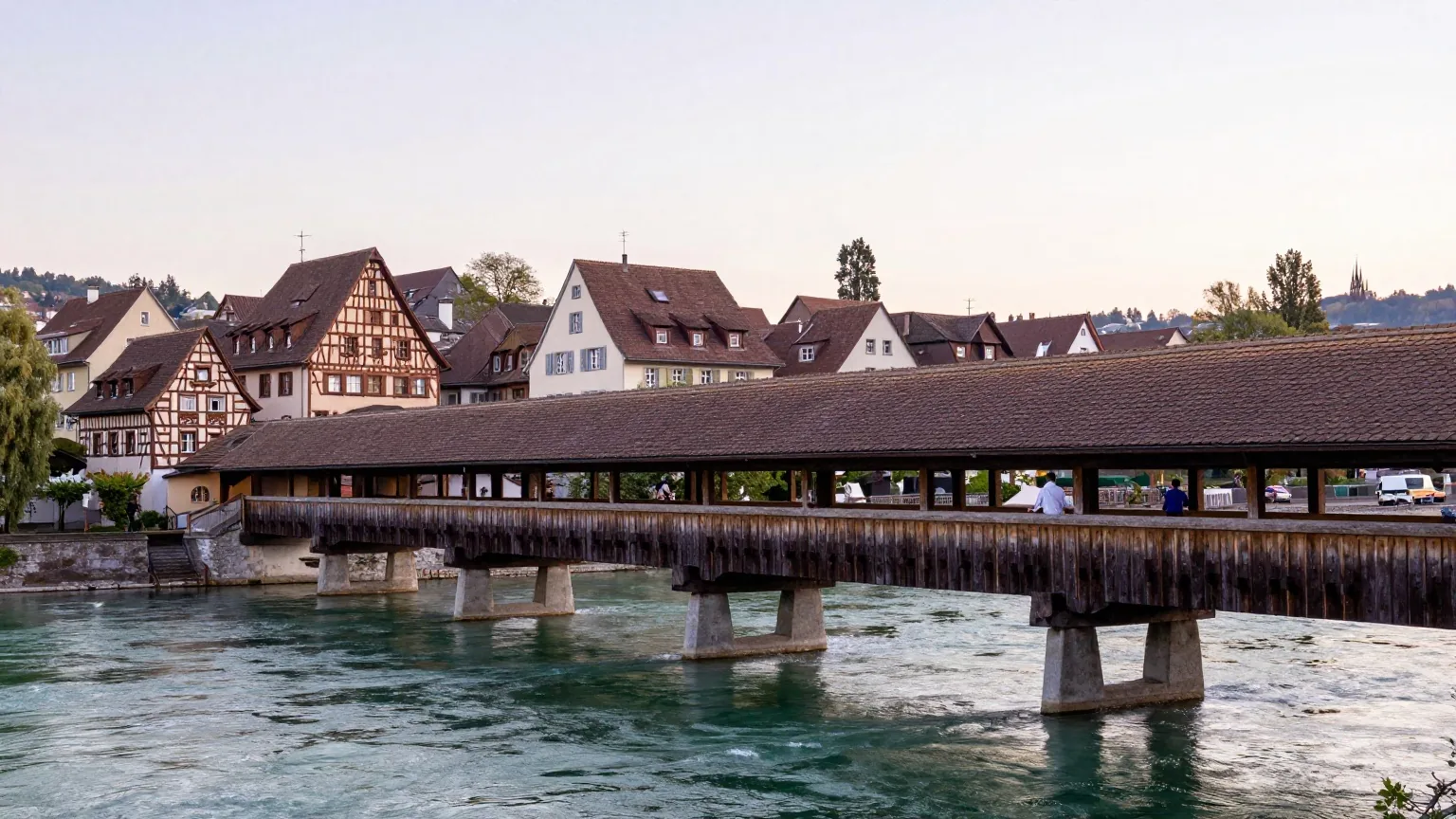 Überdachte Holzbrücke über den Rhein zwischen einer deutschen Kleinstadt und einem Schweizer Dorf, ein Radfahrer überquert sie