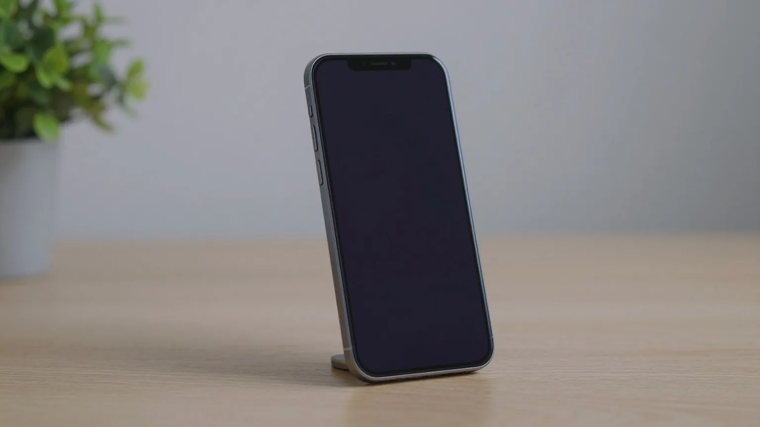 Schlankes Smartphone mit ausgeschaltetem Display steht in einem kleinen Ständer auf einem hellen Holztisch