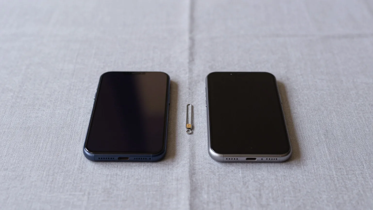 Zwei Smartphones liegen mit der Rückseite nach oben auf einer hellgrauen Leinentischdecke, dazwischen eine kleine Metallnadel